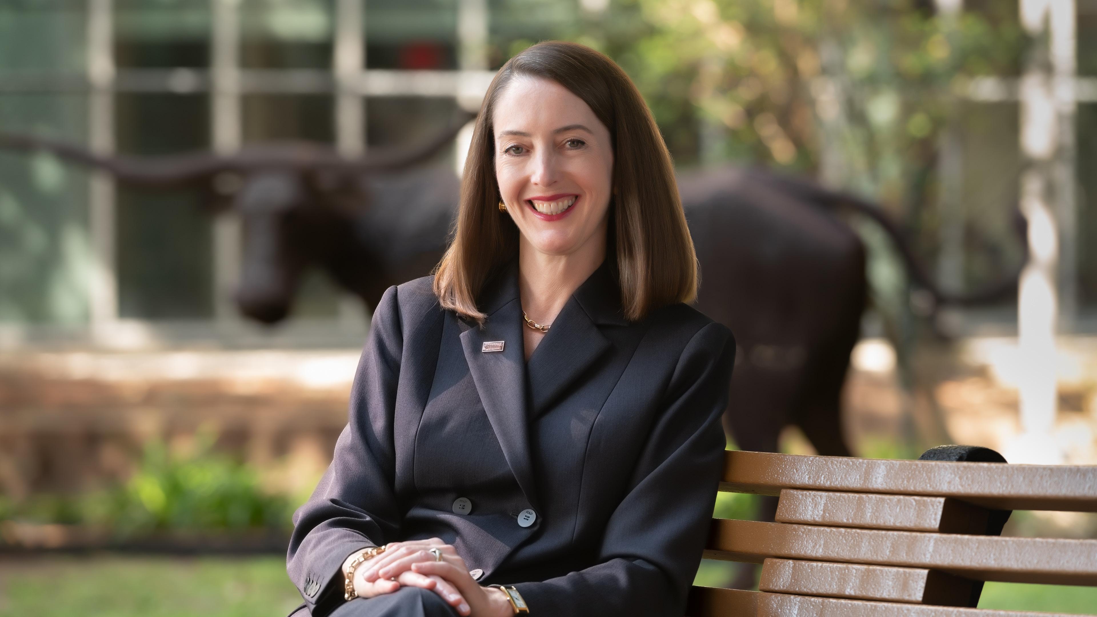 A woman sitting on a bench outside wearing a black suit.